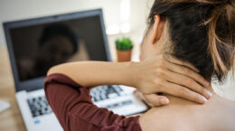Frau sitzt mit Nackenschmerzen am PC