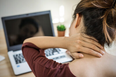 Frau sitzt mit Nackenschmerzen am PC